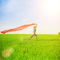 Beautiful young woman jumping on a green meadow with a colored red tissue. Royalty Free Stock Photo