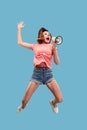 Beautiful young woman jumping with megaphone isolated over blue background Royalty Free Stock Photo