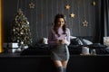 Beautiful young woman in a knitted sweater and short skirt enjoys her hot drink and posing in the Christmas interior Royalty Free Stock Photo