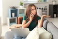 Beautiful young woman with laptop talking on mobile phone at home Royalty Free Stock Photo