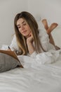 Beautiful young woman laying on bed and writing a diary in white bedroom at home. Royalty Free Stock Photo