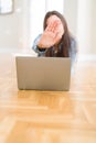 Beautiful young woman laying on the floor using laptop with open hand doing stop sign with serious and confident expression, Royalty Free Stock Photo