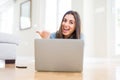 Beautiful young woman laying on the floor using laptop pointing and showing with thumb up to the side with happy face smiling Royalty Free Stock Photo