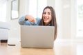 Beautiful young woman laying on the floor using laptop very happy pointing with hand and finger Royalty Free Stock Photo