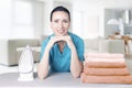 Beautiful young woman leaning on ironing board with iron and towels looking at camera and smiling while ironing clothes at home. Royalty Free Stock Photo