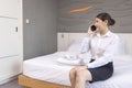 A beautiful young woman lies on a bed in a white bathrobe in a hotel, holds a telephone in her hands and dreams of something.