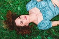 Beautiful young woman lies on green grass with loose red hair. The woman looks up dreamily Royalty Free Stock Photo