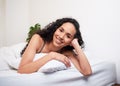 A beautiful young woman lies on her stomach on pillow in bed, smiling and happy Royalty Free Stock Photo