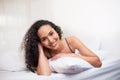 A beautiful young woman lies on her stomach on pillow in bed, smiling and happy Royalty Free Stock Photo