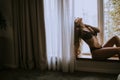 Beautiful young woman in lingerie sitting and looking outside the window in beautiful apartment Royalty Free Stock Photo