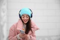 Beautiful young woman listening to music with headphones near light wall Royalty Free Stock Photo