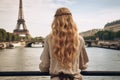 Beautiful young woman with long blond curly hair in Paris, France, Young traveler woman rear view sitting on the quay of Seine