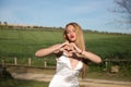 beautiful young woman with long blonde hair in white dress smiling in love making the shape of a heart symbol with her hands. Royalty Free Stock Photo