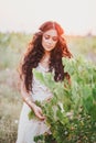 Beautiful young woman with long curly hair dressed in boho style dress posing in a field with dandelions Royalty Free Stock Photo