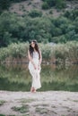 Beautiful young woman with long curly hair dressed in boho style dress posing near lake Royalty Free Stock Photo