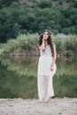 Beautiful young woman with long curly hair dressed in boho style dress posing near lake Royalty Free Stock Photo