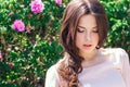 Beautiful young woman with long curly hair posing near roses in a garden. The concept of perfume advertising. Royalty Free Stock Photo