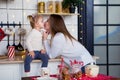 Beautiful young woman with long hair kisses a little daughter in a white sweater in the kitchen. christmas home decor