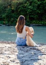 Beautiful young woman with long hair sitting on sand hugging dog near the river enjoying the silence