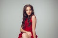 Beautiful young woman with long healthy curly hair and bright make up wearing red dress  on grey studio Royalty Free Stock Photo