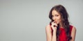 Beautiful young woman with long healthy curly hair and bright make up wearing red dress  on grey studio Royalty Free Stock Photo