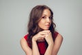 Beautiful young woman with long healthy curly hair and bright make up wearing red dress  on grey studio Royalty Free Stock Photo