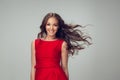 Beautiful young woman with long healthy curly hair and bright make up wearing red dress  on grey studio Royalty Free Stock Photo