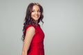 Beautiful young woman with long healthy curly hair and bright make up wearing red dress  on grey studio Royalty Free Stock Photo