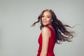 Beautiful young woman with long healthy curly hair and bright make up wearing red dress  on grey studio Royalty Free Stock Photo