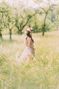 Beautiful young woman in long lilac dress with wreath on head standing back outdoors