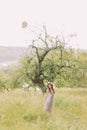 Beautiful young woman in long lilac dress with wreath on head standing near tree