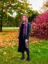 Beautiful young woman with long pink dreadlocks in black dress, biker jacket and sneakers posing in the park on the grass in Royalty Free Stock Photo