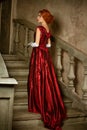 A beautiful young woman in a long red retro dress is standing on the stairs Royalty Free Stock Photo