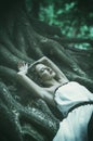 beautiful young woman in a long white dress with long wavy hair, lying on the large roots of a tree with his eyes closed Fairy ta Royalty Free Stock Photo