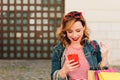 Beautiful and young woman looking at her phone while shopping on summer sales, with many colorful bags Royalty Free Stock Photo