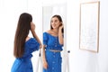 Beautiful young woman looking at herself in mirror indoors Royalty Free Stock Photo