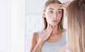 Beautiful young woman looking in a mirror and touching her face Royalty Free Stock Photo