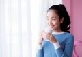 Beautiful young woman is looking out the window and holding a cup of coffee in morning. Royalty Free Stock Photo