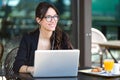 Beautiful young woman looking sideways while working with her laptop in a coffee shop.