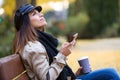 Beautiful young woman looking to sky while using her mobile phone and sitting in a bench in the street Royalty Free Stock Photo