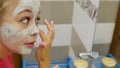 Beautiful young woman looks in the mirror and applies a cosmetic face mask. A pretty blonde in curlers on her head is Royalty Free Stock Photo