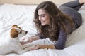 beautiful young woman lying on bed with her cute small dog besides. Home, indoors and lifestyle Royalty Free Stock Photo