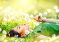 Beautiful young woman lying on the field in green grass and blowing dandelion flowers
