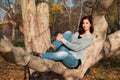 A beautiful young woman is lying in a relaxed pose on a tree. In background of autumn landscape