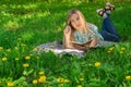 Beautiful young woman lying and writing in her diary on the grass with flowers. Front view. Royalty Free Stock Photo