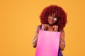 Afro american woman at shopping holding pink bag isolated on orange background on black friday holiday. Copy space for Royalty Free Stock Photo