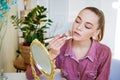 Beautiful young woman makes blush on her face using makeup brush while sitting Royalty Free Stock Photo