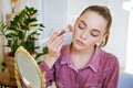 Beautiful young woman makes blush on her face using makeup brush while sitting Royalty Free Stock Photo