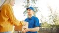 Beautiful Young Woman Meets Delivery Man who Gives Her Cardboard Box Package, She Signs Electronic Royalty Free Stock Photo