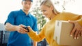 Beautiful Young Woman Meets Delivery Man who Gives Her Cardboard Box Package, She Signs Electronic Royalty Free Stock Photo